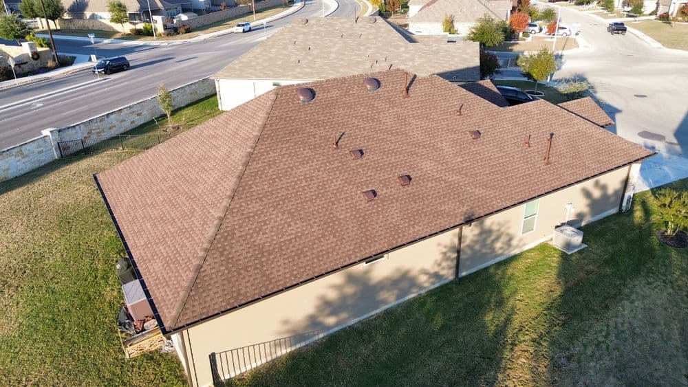 Aerial view of a modern home with a brown shingle roof and manicured lawn.