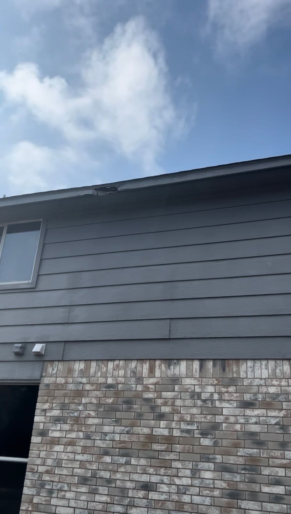 Gray house exterior with brick details and cloudy sky above.